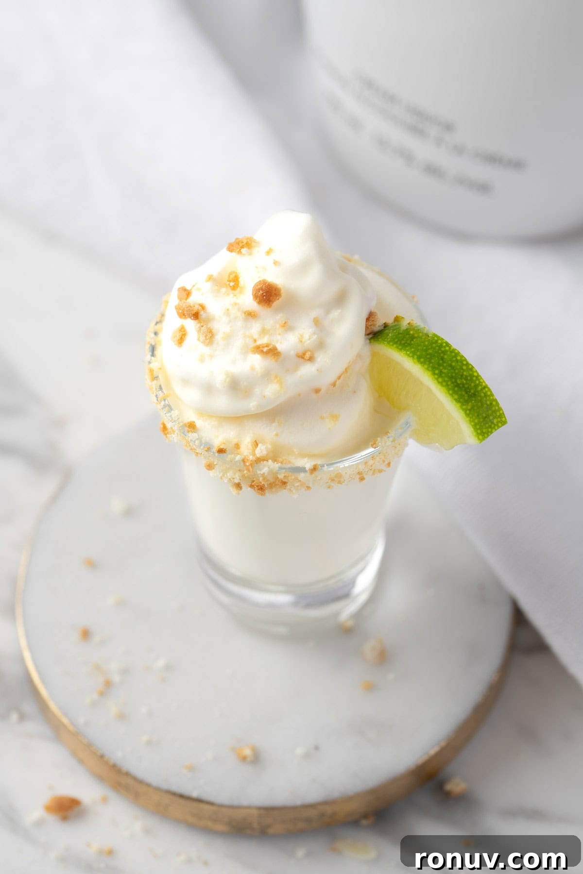 Key Lime Pie Shot Recipe: Creamy Citrus Shooter 6 A Key Lime Pie Shot on a white and gold coaster.