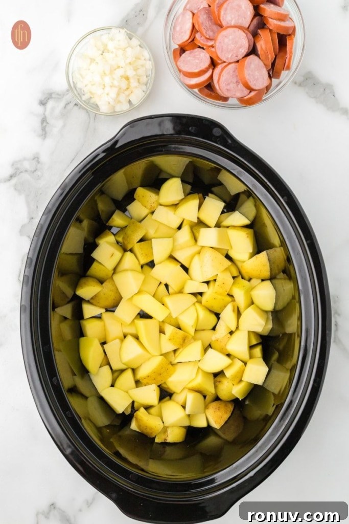 Slow Cooker Sausage and Potatoes 6 a prep image of a crockpot full of cubed potatoes with a bowl of sausage and chopped onions next to it.