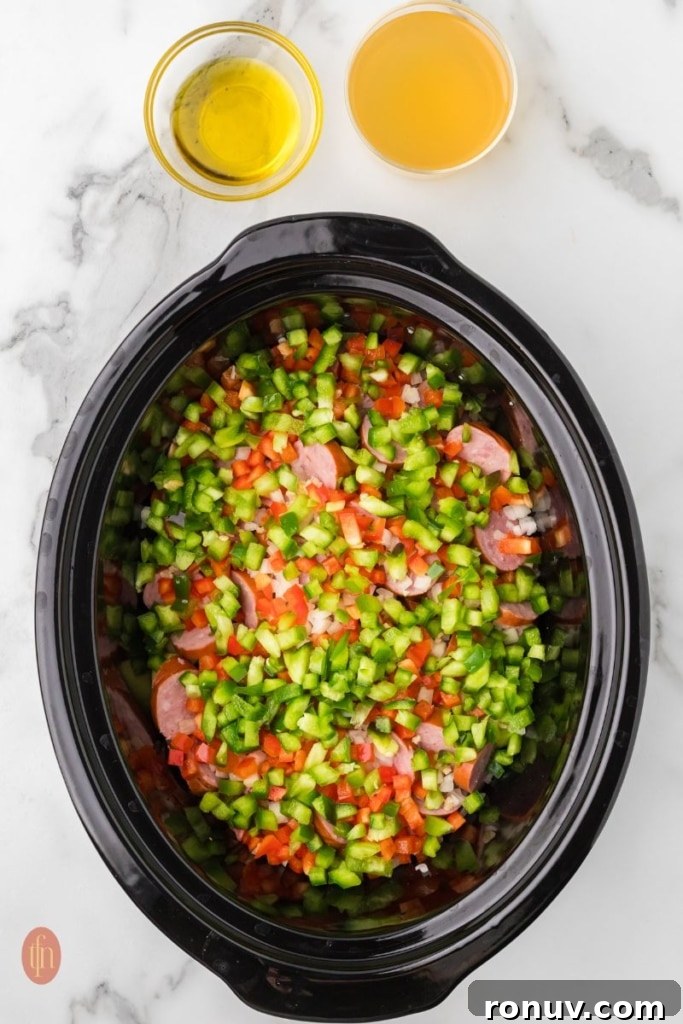 Slow Cooker Sausage and Potatoes 8 a prep image of a crockpot full of cubed potatoes, sausage, onion, red bell pepper, green bell pepper, and garlic with bowls of broth and oil next to it.