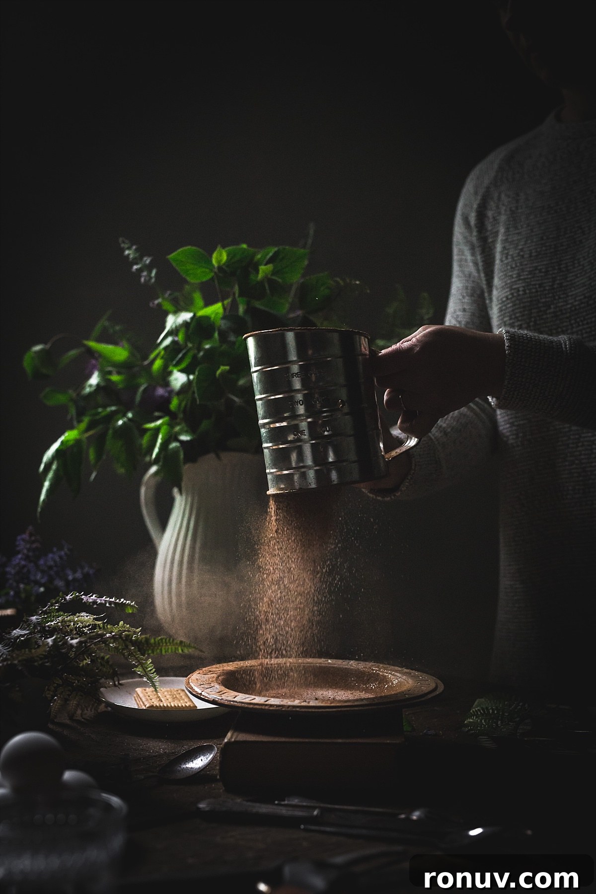 Kalter Hund Recipe: German No-Bake Layered Chocolate Cookie Cake 6 Backlit image of sifting cocoa powder and sugar into a decorative bowl.