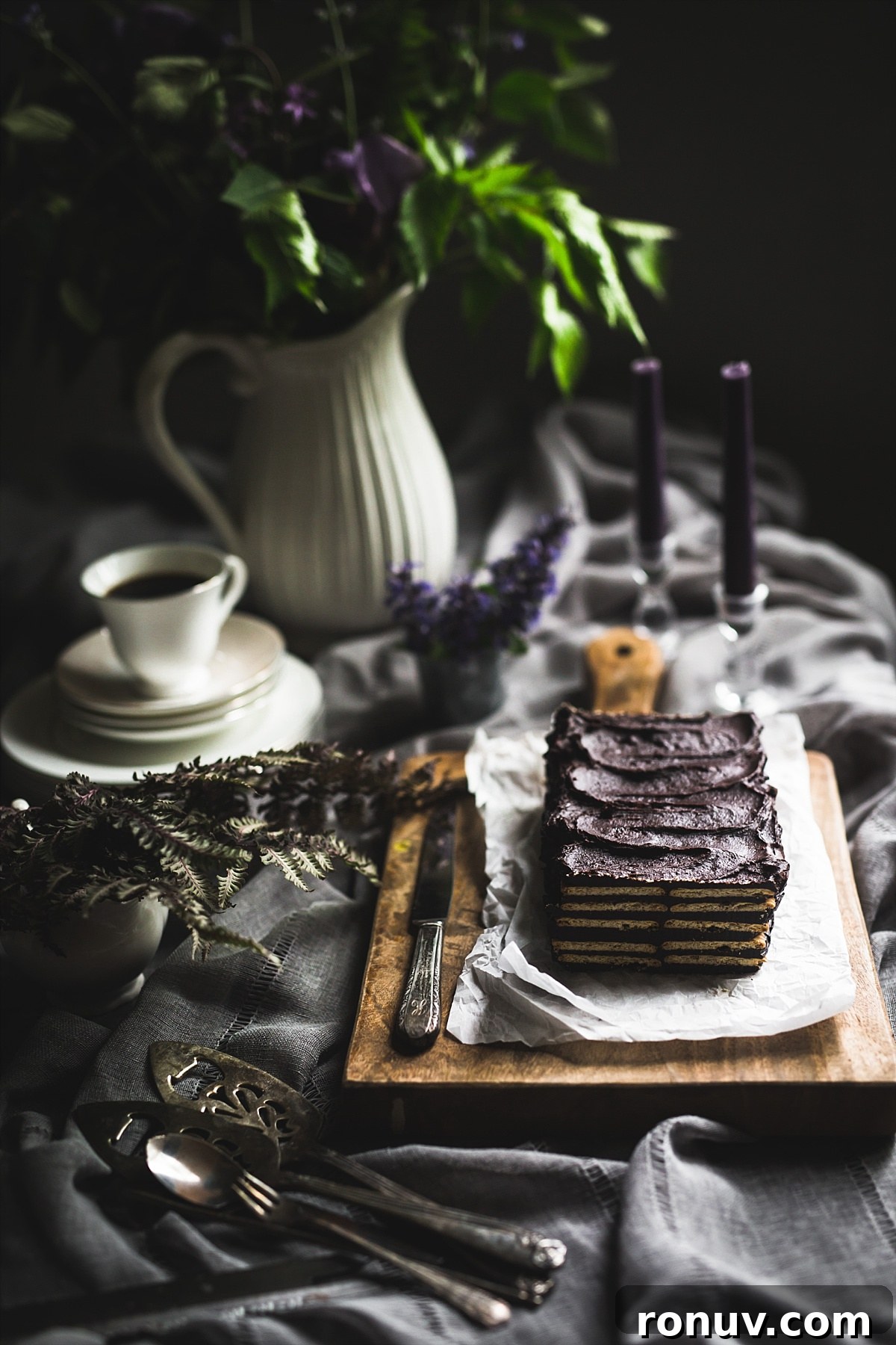 Kalter Hund Recipe: German No-Bake Layered Chocolate Cookie Cake 9 Backlit image of no bake layered Kalter Hund that has a slice taken out of it so you can see the layers of the cake. It is sitting on paper that is on top of a wooden cutting board.