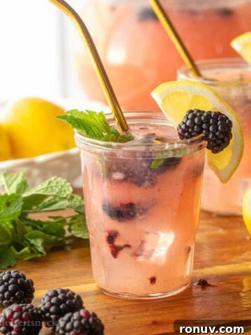 Glass of blackberry pear lemonade on wood board with straw.