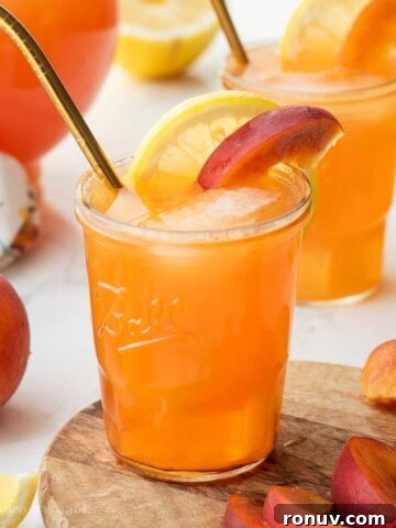Glass of peach lemonade with slices of lemon and peach and straw.