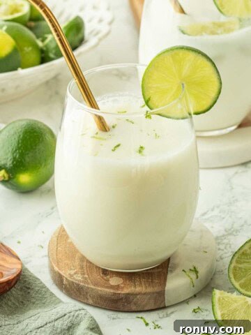 Brazilian limeade in glass cup with gold straw and lime slice on edge on marble coaster.