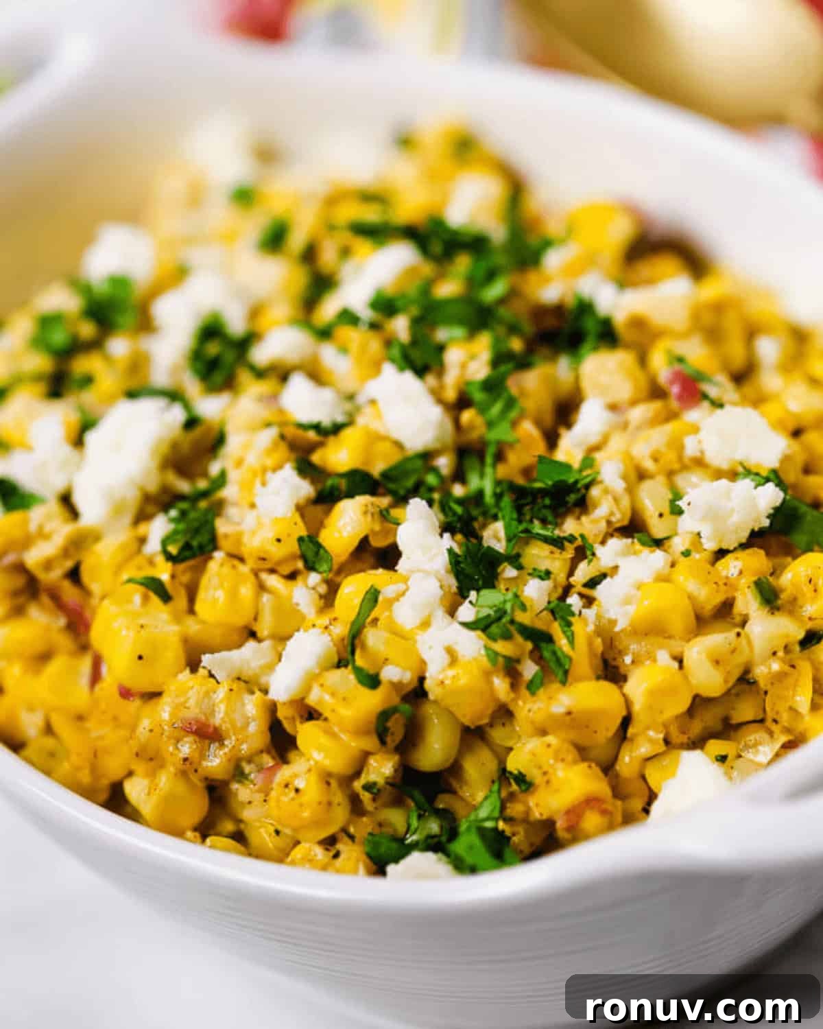Elote Salad: Mexican Street Corn Recipe 2 A white bowl filled with flavorful Elote Salad—seasoned corn topped with crumbled cheese and chopped fresh herbs.