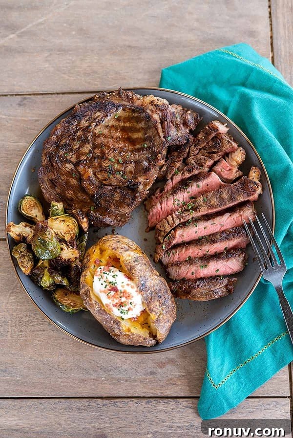 plate of grilled ribeye steak on gray plate with baked potato and grilled brussels sprouts.