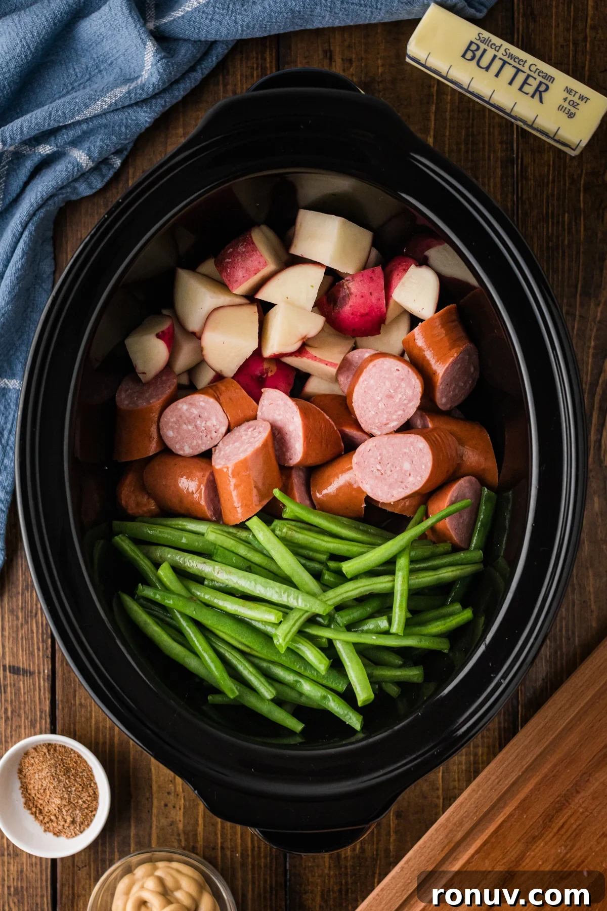 Slow Cooker Kielbasa Dinner Recipe with Potatoes 4 Potatoes, kielbasa, and green beans arranged separately in a crockpot.