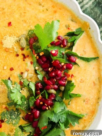 Pumpkin carrot soup in a scalloped bowl with parsley and pomegranate on the side.