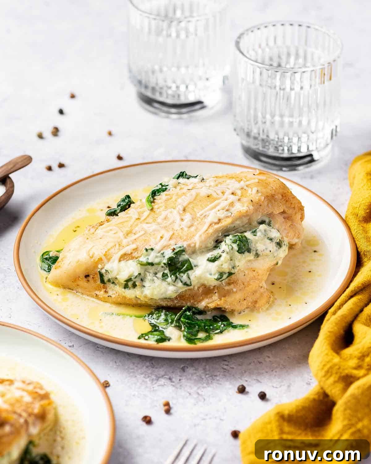 Spinach and Cheese Stuffed Chicken Florentine 16 A plate of stuffed chicken florentine in front of glasses of water.