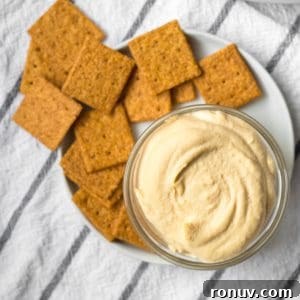 homemade hummus in a small glass dish with wheat crackers on a plate