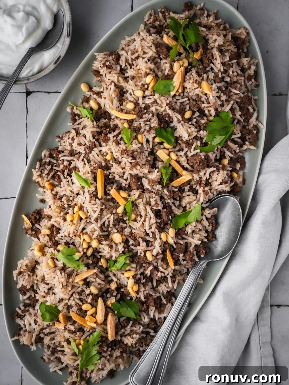 Lebanese Hashweh: Spiced Rice with Ground Beef 2 Platter with hashweh spiced rice with ground beef garnished with parsley and toasted nuts with a side of plain yogurt.