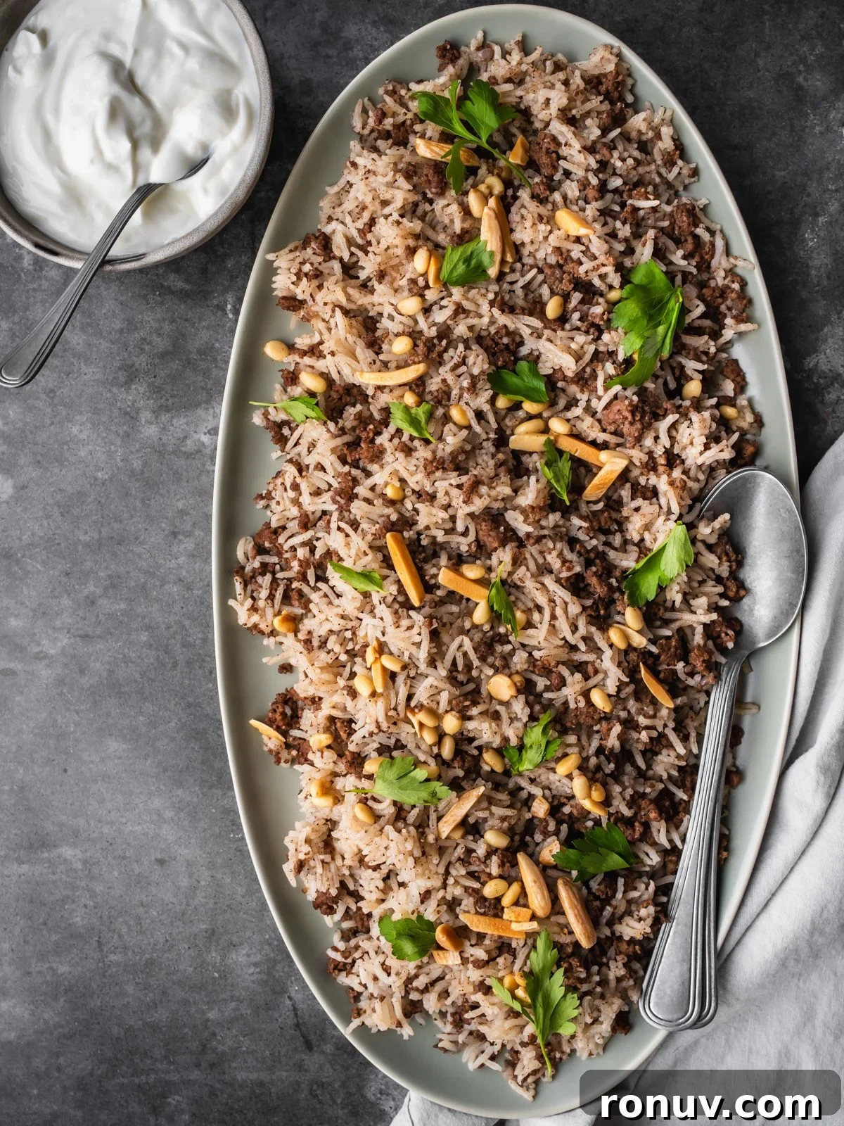 Lebanese Hashweh: Spiced Rice with Ground Beef 12 Platter with hashweh spiced rice with ground beef garnished with parsley and toasted nuts with a side of plain yogurt.