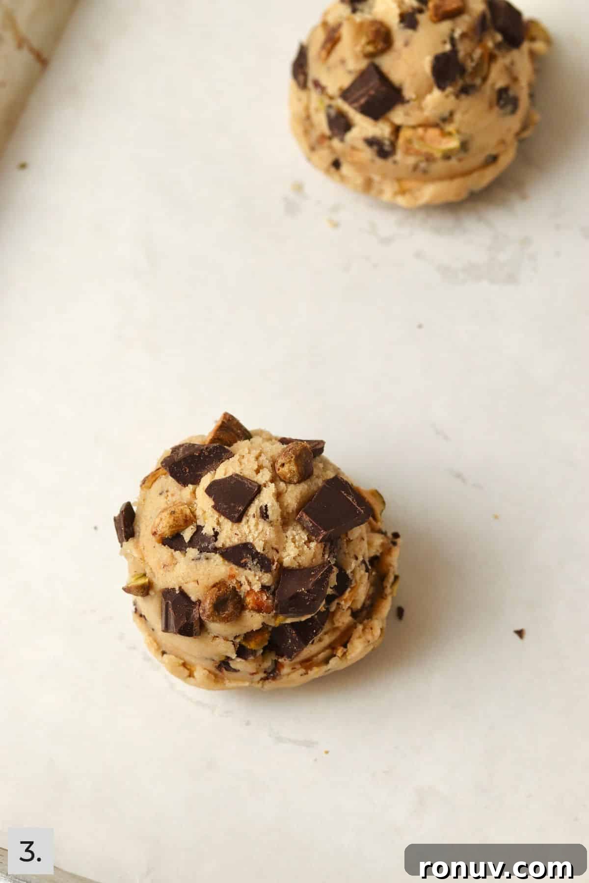 Two unbaked pistachio chocolate chunk cookies on a baking sheet.