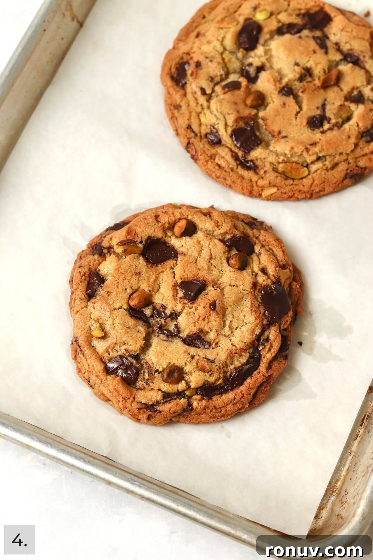 Two baked pistachio chocolate chunk cookies on a baking sheet.
