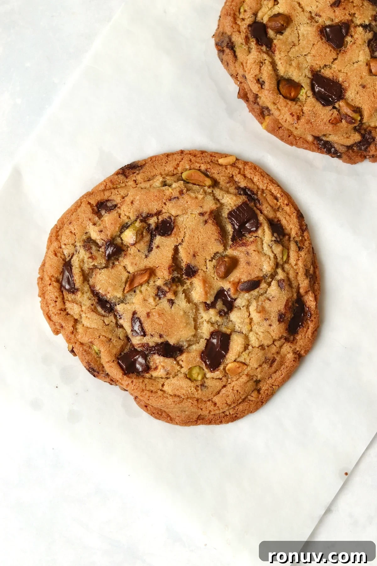 Baked single serve pistachio chocolate chunk cookie on parchment paper.