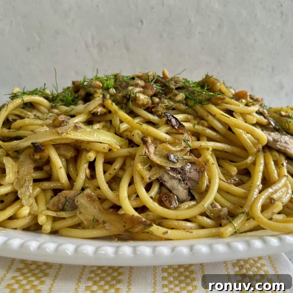Authentic Sicilian Pasta con Sarde Recipe 8 Side view of finished Sicilian pasta con sarde recipe with fennel fronds garnish on white platter over decorative towel.