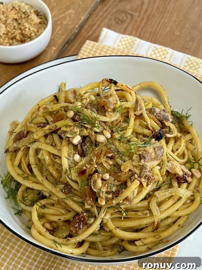 Authentic Sicilian Pasta con Sarde Recipe 9 Sicilian sardine pasta in white bowl over decorative towel with small dish of toasted breadcrumbs in the background.