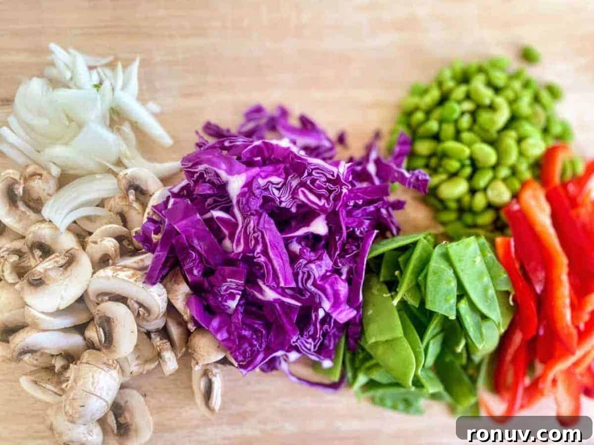 15-Minute Garlic Butter Noodles Recipe 3 Onions, mushrooms, red cabbage, pea pods, mame and red peppers on a cutting board.