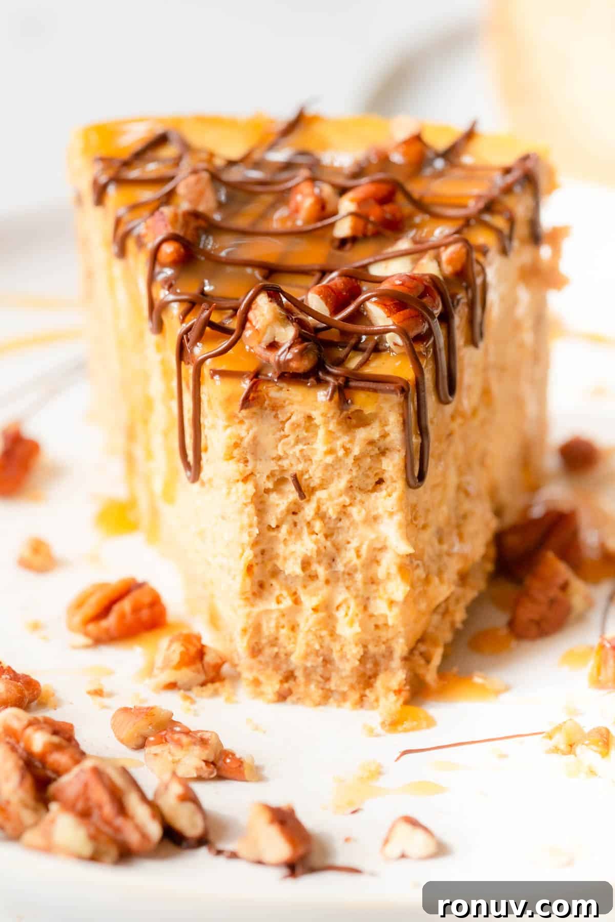 Turtle-Topped Pumpkin Cheesecake Recipe 5 A slice of Turtle Pumpkin Cheesecake on a white plate with chopped pecans scattered around.