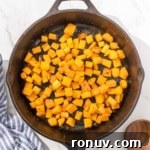 Cubed butternut squash in a skillet on a marble countertop.