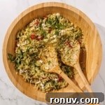 A wooden bowl filled with orzo pesto salad mixed with arugula and feta.