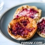 Three English muffins with butter and jam sit on a blue plate.