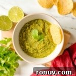 A bowl of serrano salsa with limes, chips, and cilantro.