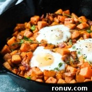 A cast iron skillet containing sweet potato hash with bacon and sunny-side-up eggs.