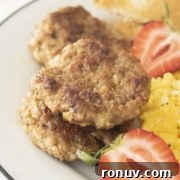 A plate containing sausage patties, scrambled eggs, sliced strawberries, and bread.