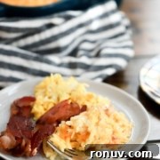 A plate of scrambled eggs, hash browns, and bacon with a striped cloth and baking dish.