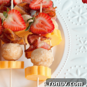 Skewers with strawberries, cheese cubes, bacon pieces, and doughnut holes on a plate.