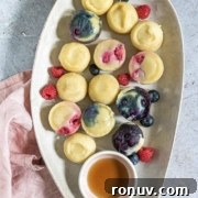 Platter of assorted mini berry cheesecakes and fresh berries with a small bowl of syrup.