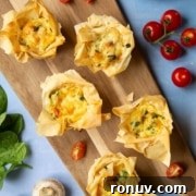 A wooden board with filo pastry tartlets filled with vegetables and cheese.