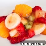 A plate of fruit salad with banana slices, strawberries, kiwi, and orange segments.