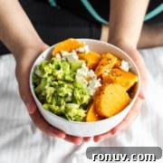 Person holding a bowl containing avocado mash, feta cheese, and sliced sweet potatoes.