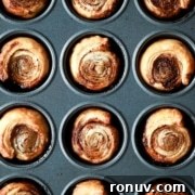 A muffin tin filled with twelve baked cinnamon rolls with golden-brown tops.