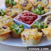 A white plate with hash brown and cheese cups, kiwi pieces, and a bowl of salsa.