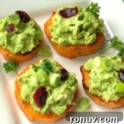 A white plate with sweet potato slices topped with avocado and garnishes.
