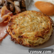 A close-up of a breakfast plate featuring a hash brown patty, fried egg, mushrooms, and bacon.