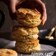 A hand stacking three golden-brown biscuits on parchment paper.