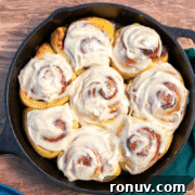 A cast iron skillet filled with eight frosted cinnamon rolls.