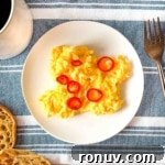 Chilli scrambled eggs on a white plate surrounded by a cup of coffee and English muffins.