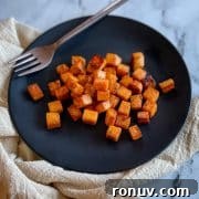 Cubed, sautéed sweet potatoes on a black plate with a gold fork.