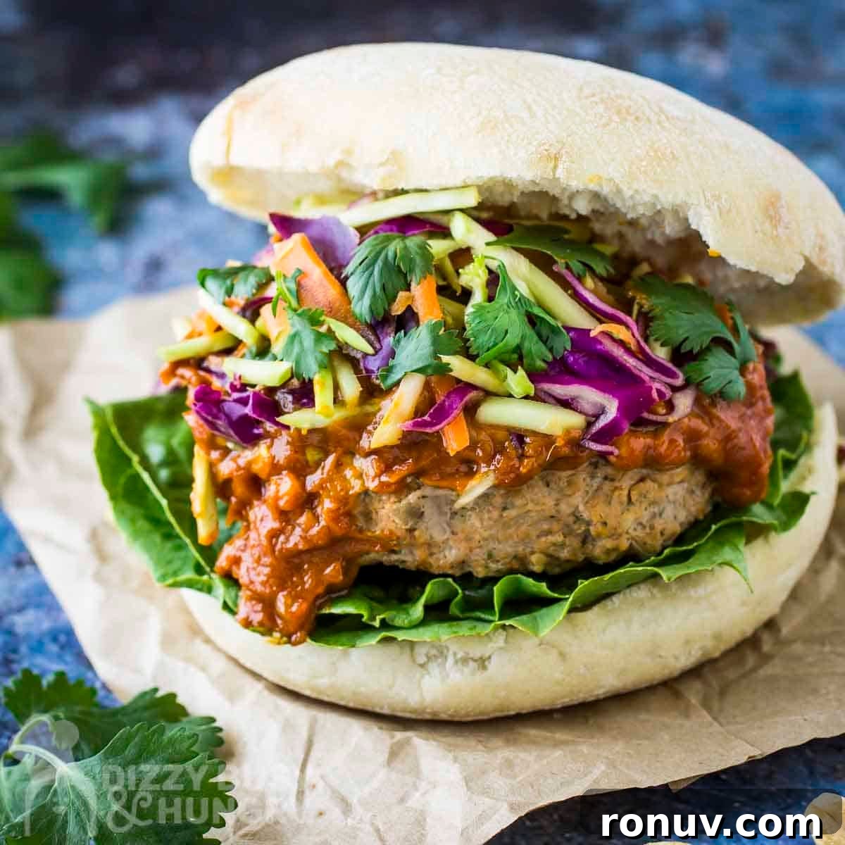 Thai Turkey Burgers with Sweet Chili Glaze 2 Side close up shot of thai turkey burger garnished with fresh parsley on a piece of brown parchment paper.