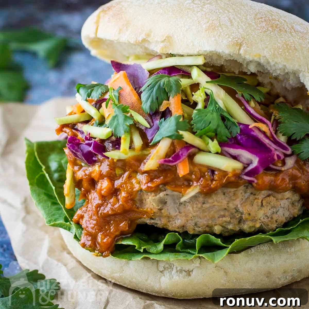 Thai Turkey Burgers with Sweet Chili Glaze 12 Side close up shot of thai turkey burger garnished with fresh parsley on a piece of brown parchment paper.
