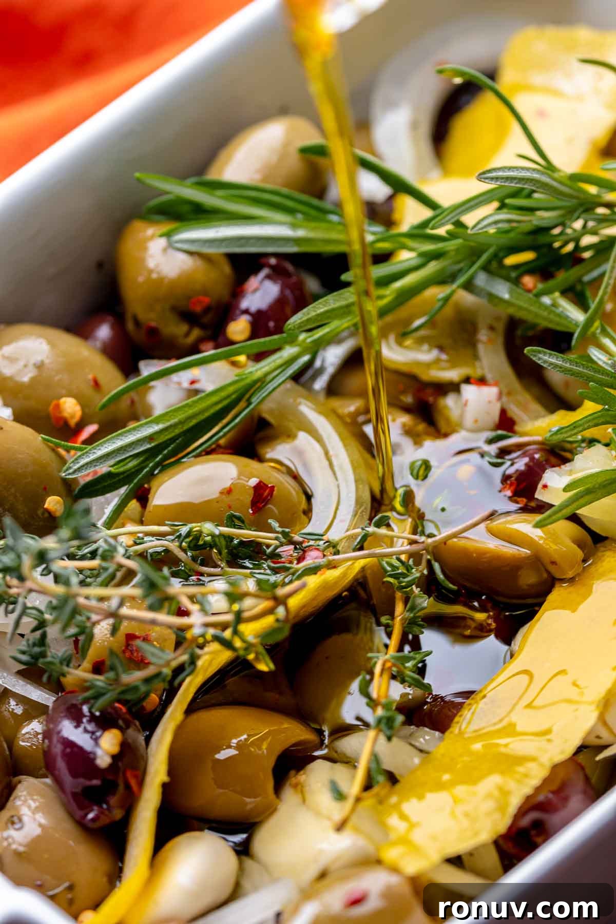 Herb Roasted Olives with Burrata Recipe 7 Olive oil being poured on top of olives in a baking dish.
