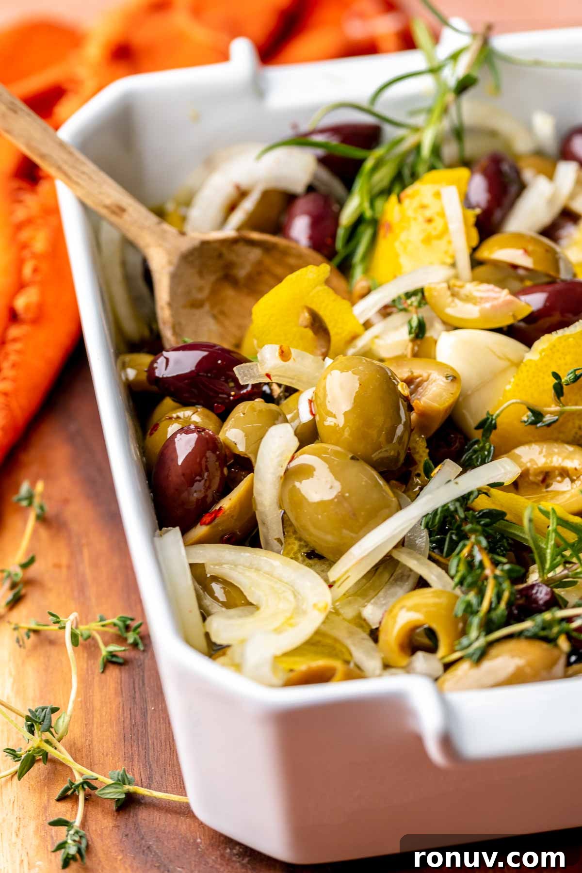 Herb Roasted Olives with Burrata Recipe 8 A spoon stirs olive mixture in a baking dish.