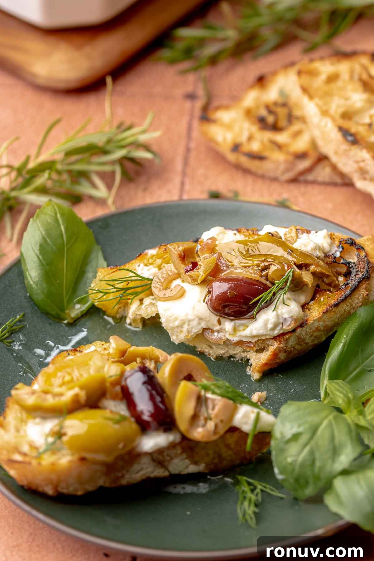 Herb Roasted Olives with Burrata Recipe 10 Burrata and roasted olives on a piece of toast on a plate.