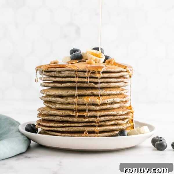 Tall stack of buckwheat pancakes topped with blueberries and maple syrup.
