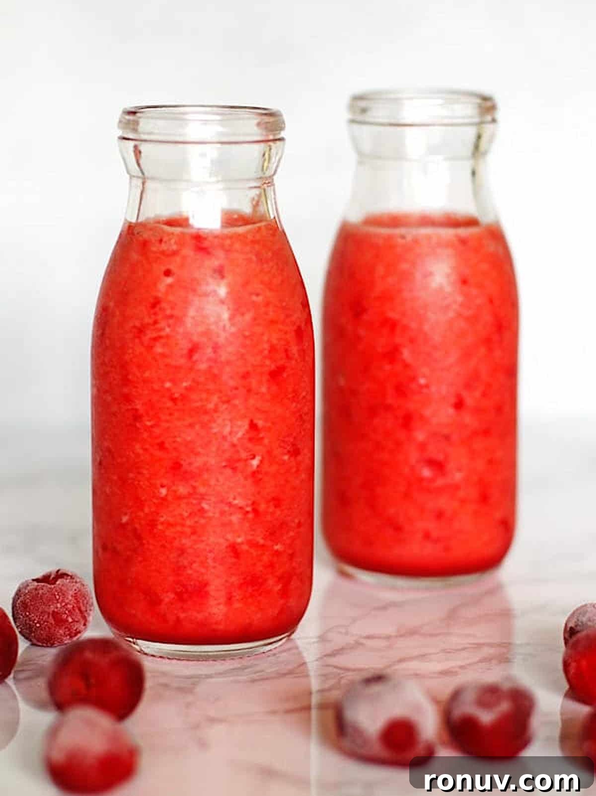 Cherry Smoothie in two clear glasses with frozen cherries on the counter next to the glasses